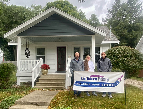 A photo of the 2023 winners of Operation Community Refresh stand in front of their home with a banner of the event.
