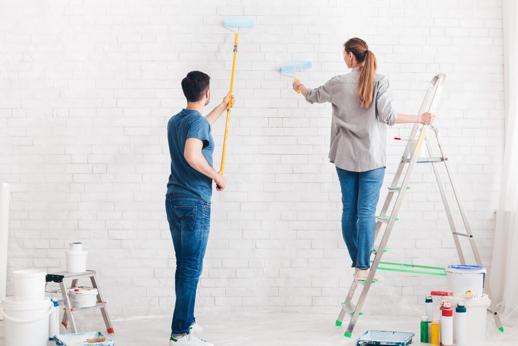 A couple of interior wall painters work on painting a white brick wall.