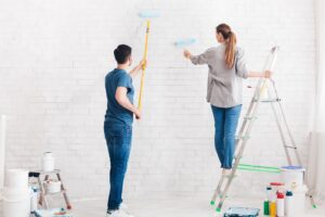 A couple of interior wall painters work on painting a white brick wall.