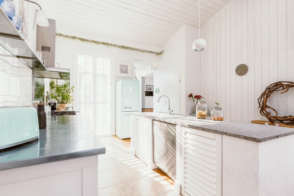 A rustic kitchen with white furniture and white wooden walls.