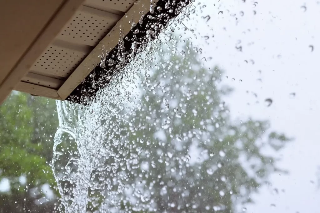 During a downpour, water escapes over the bottom edge of a gutter.