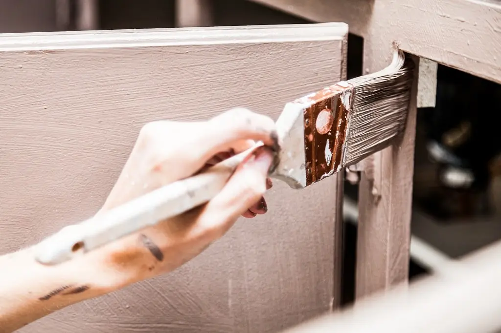 Closeup of a hand with a paint brush painting kitchen cabinets.
