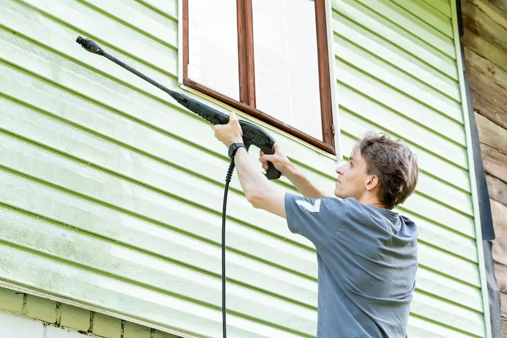 A young man washes the facade of a country house with a power washer.