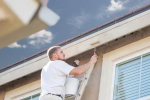 Professional painter using a small roller to paint the side of a home.