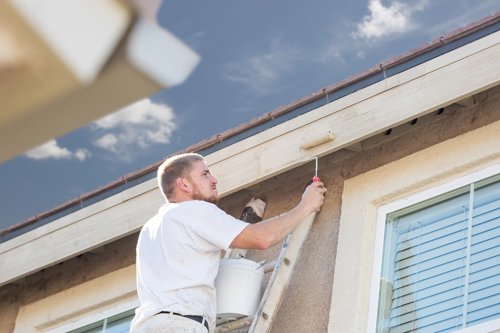 Professional painter using a small roller to paint the side of a home.
