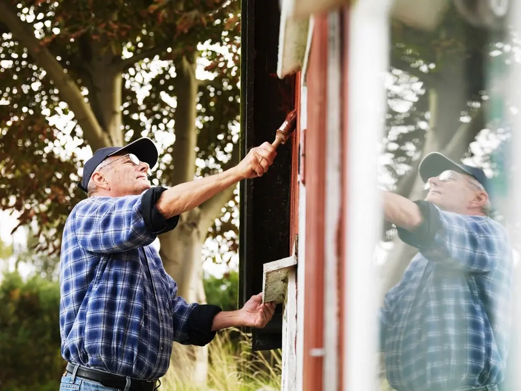 An older man painting the side of a house.