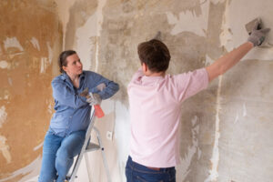 Young couple removing old wallpaper from walls preparing for flat renovation.