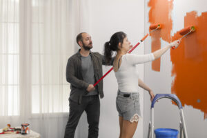 Family using orange color to paint wall with roller and paintbrush during home renovation. Painting with new color to redecorate apartment room, interior renovation and house improvement.